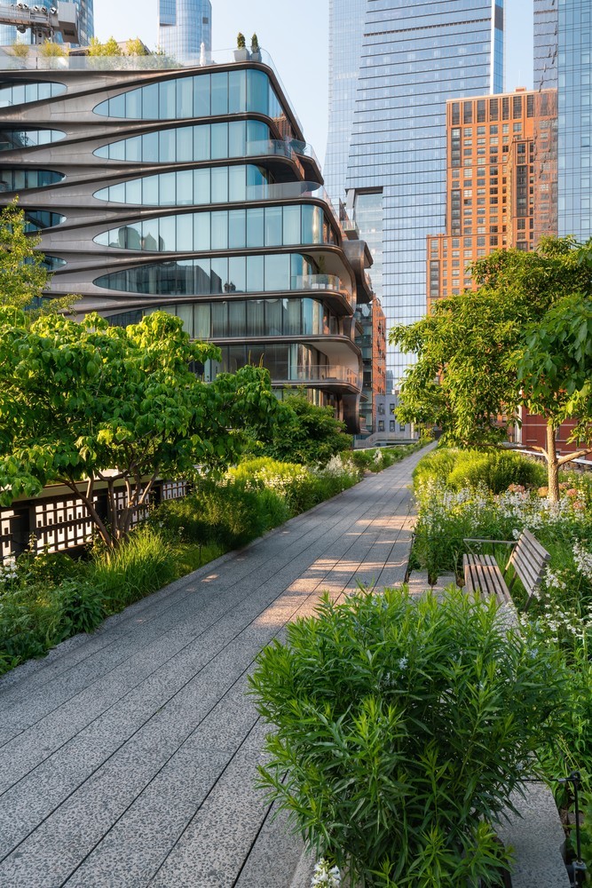 People walking along the High Line park surrounded by greenery and city views.