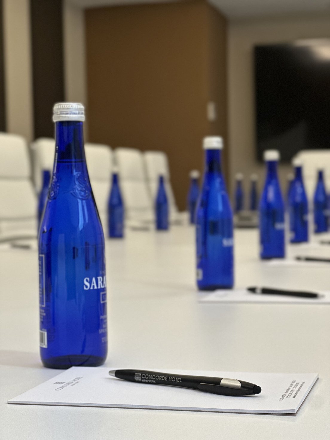 Blue glass water bottles and branded notepads on a white conference table in a modern meeting room