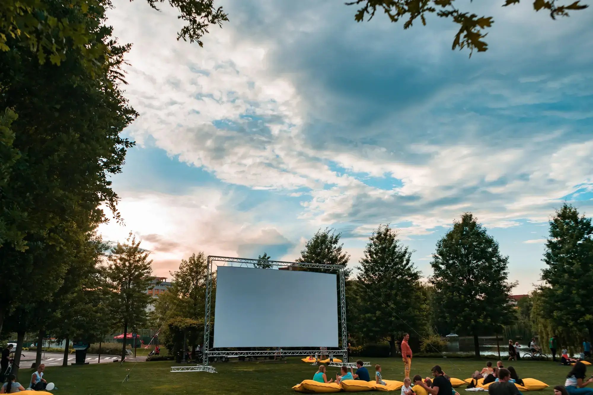 People enjoying an open-air cinema surrounded by lush greenery and a beautiful sunset.