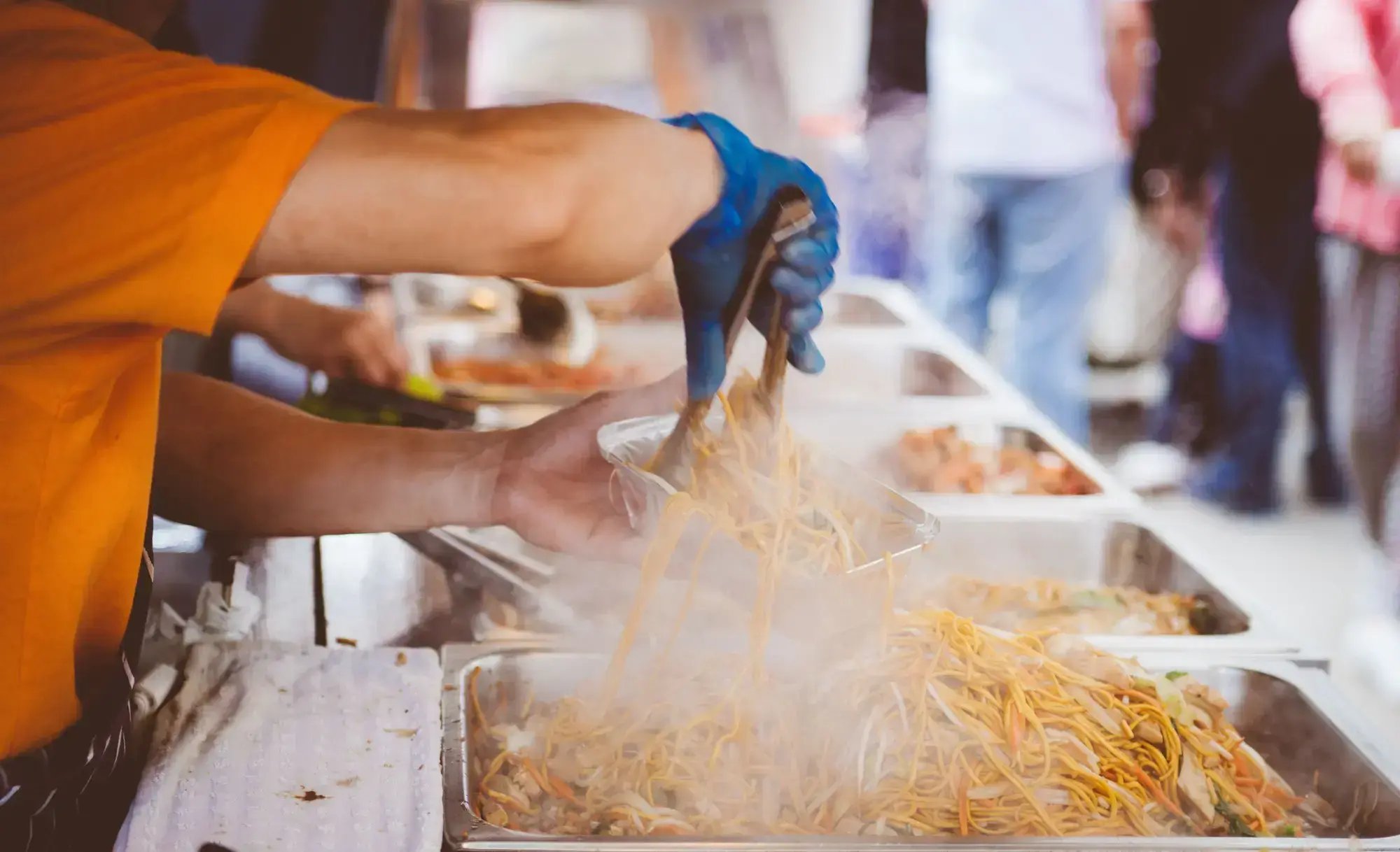 A street vendor serving freshly cooked noodles at a bustling outdoor market