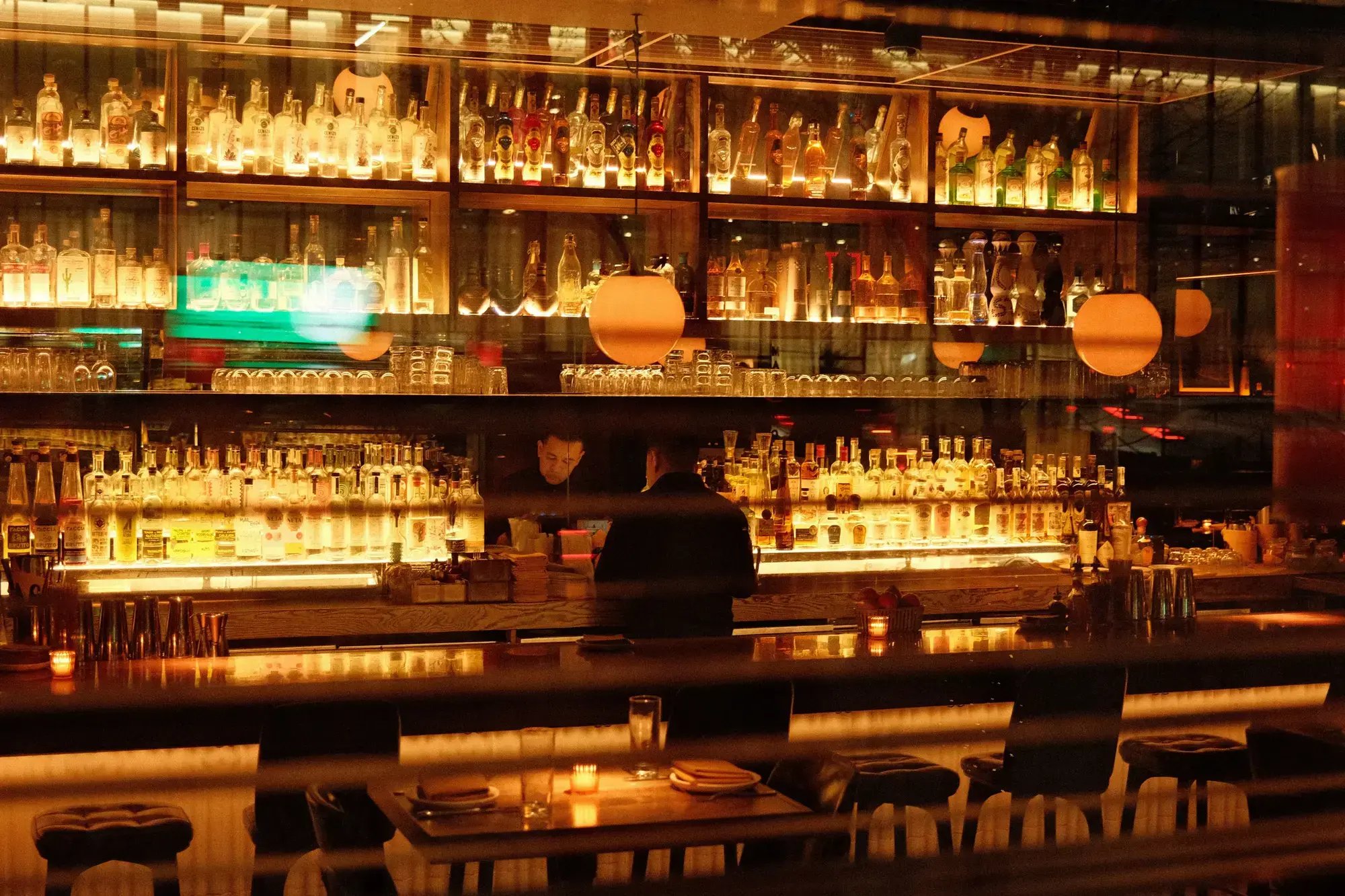 Warm and inviting bar interior in New York, featuring illuminated shelves of bottles and soft ambient lighting