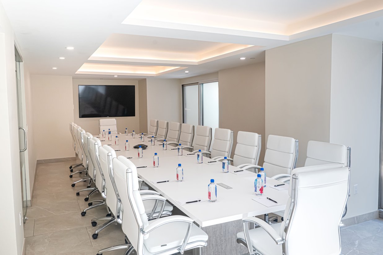 Modern conference room with white chairs, table, bottled water, and large screen.