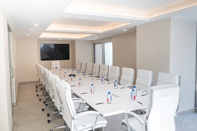 Modern conference room with white chairs, table, bottled water, and large screen.