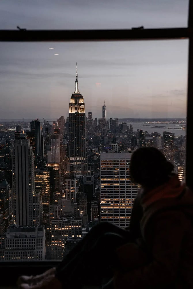 A woman watching new york city silhouette from a skyscraper.