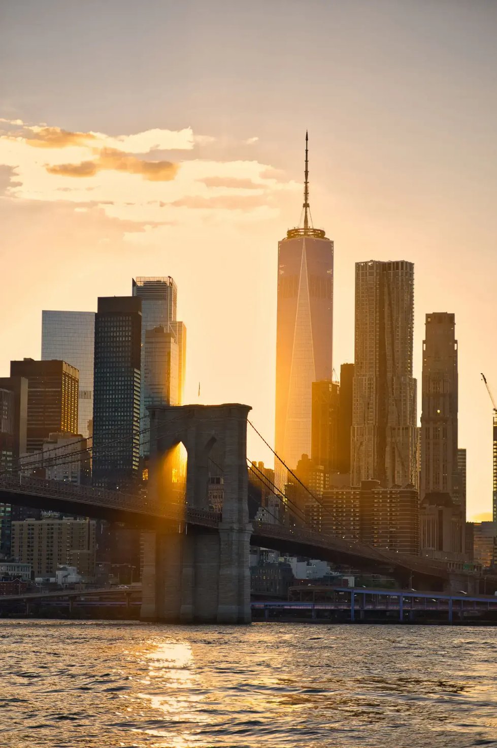 view of Brooklyn Bridge and New York City skyline during sunset with golden light.