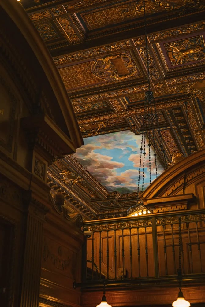 Intricate decorated ceiling in the New York Public Library with classic architecture and cloud mural.
