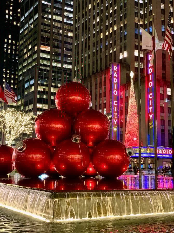 Giant red Christmas ornament spheres displayed in front of Radio City Music Hall in New York City.